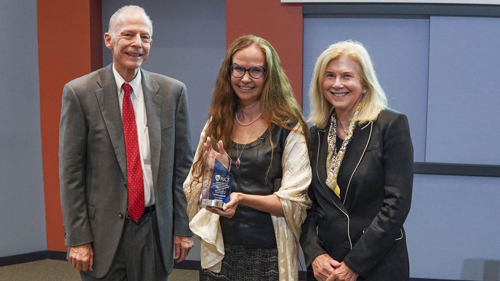 Three people standing in a row holding an award